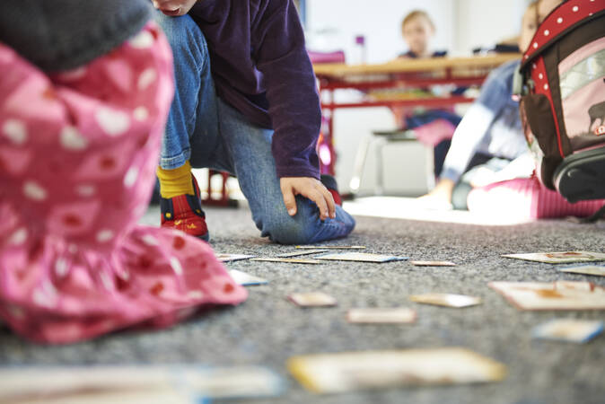 Auf einem grauen Teppich sind Spielkarten ausgelegt, ein Kind in lila T-Shirt spielt damit.