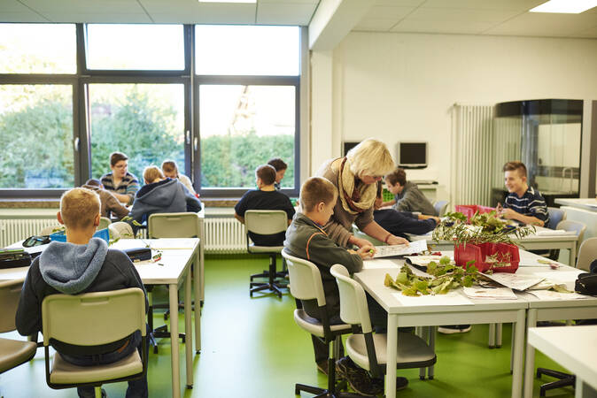 Ein Klassenzimmer mit mehreren Schülern an Gruppentischen und Lehrpersonal.