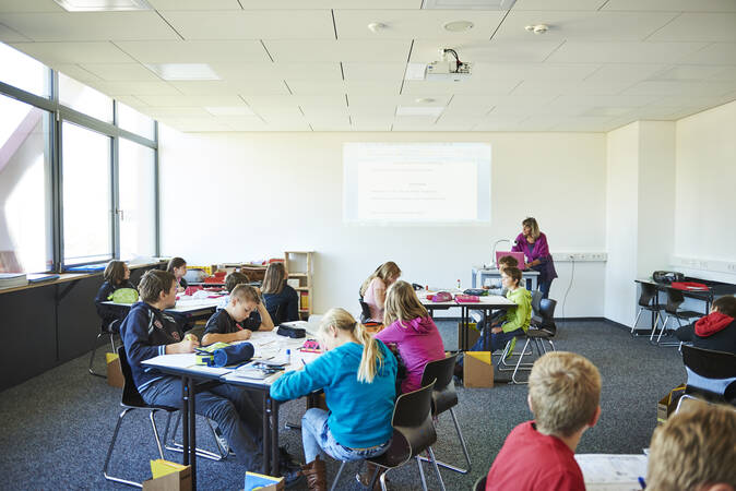 Ein Klassenzimmer mit mehreren Schülern an Gruppentischen und Lehrpersonal.