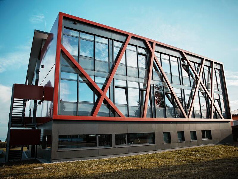 Ein modernes kastenförmiges Gebäude mit großen Glaselementen erstrahlt in den Farben grau und rot.